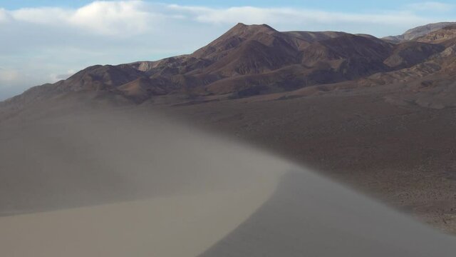 Sand blowing by strong wind creating a dune and mountains and clouds in the background, Eureka Dunes, Death Valley National Park
