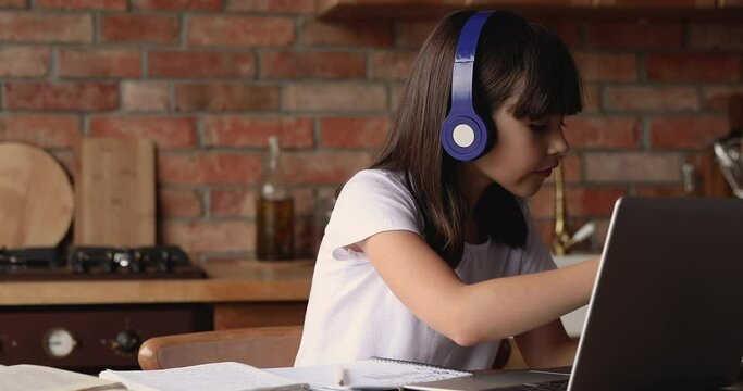 Little cute girl wear headphones listen tutor take notes study language online use video call application on laptop. Younger z gen and modern tech easy comfort usage, quarantine home-schooling concept