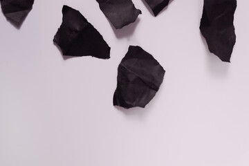 at the top of the photo of a black crumpled paper cat lie on a white surface