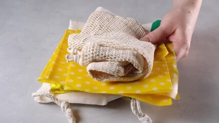 Zero waste concept. Using cotton bags instead of foil, cling film and plastic containers. Female hand pushing away plastic packs and placing cotton bags, wax cloth on a table. Plastic free. 4K UHD