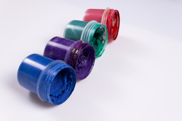 side view and slightly from above on four jars of gouache in different colors of blue, lilac, green, red