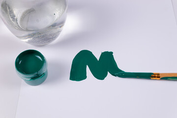 a green jar of gouache is open, next to a transparent jar, and a smear of green paint and a brush at the end, top view