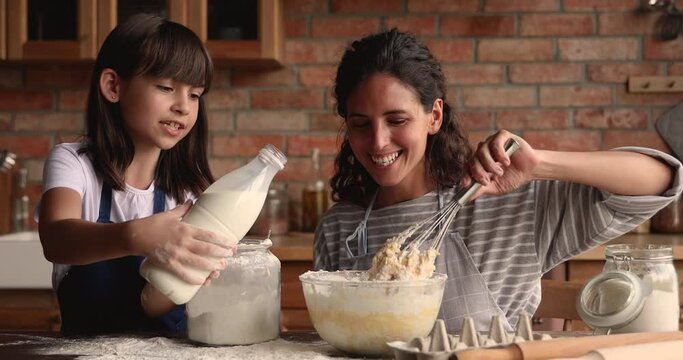 Young woman teach little 10s daughter cooking in cozy kitchen, preparing family recipe pie together, add milk and flour making dough for cake. Hobby, develop of child, share skills, motherhood concept