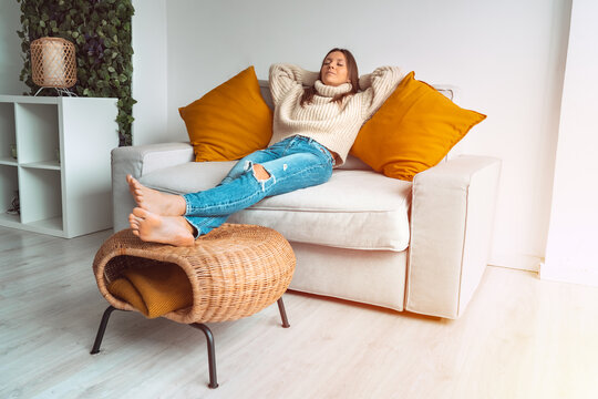 Calm satisfied and relaxed woman in cozy sweater resting or sleeping on the sofa in the living room. Enjoying break with eyes closed, peace of mind, no stress. Day off work