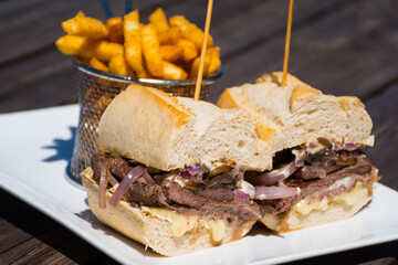 A steak sandwich and fries served on a white plate