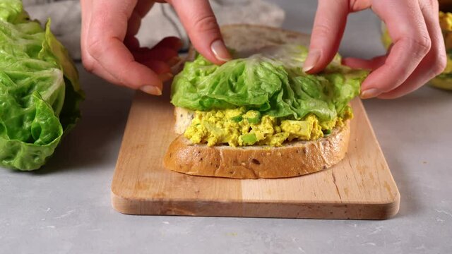 Woman hands making vegan sandwich club with sourdough bread and bright yellow vegan egg salad made from tofu. Healthy organic vegan food. 4K UHD