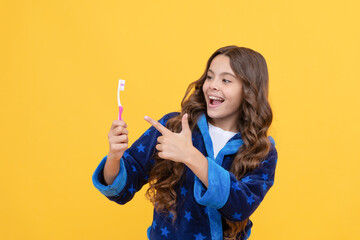 happy child girl in cozy bathrobe pointing finger on toothbrush in morning, dental care
