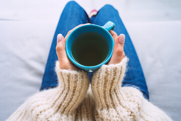 Woman in woolen cozy sweater warming cold hands with a mug of hot tea. Woman holding cup of tea.