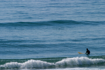 A surfer lying on his surfboard paddles over an approaching wave on a beach in Portugal on the...