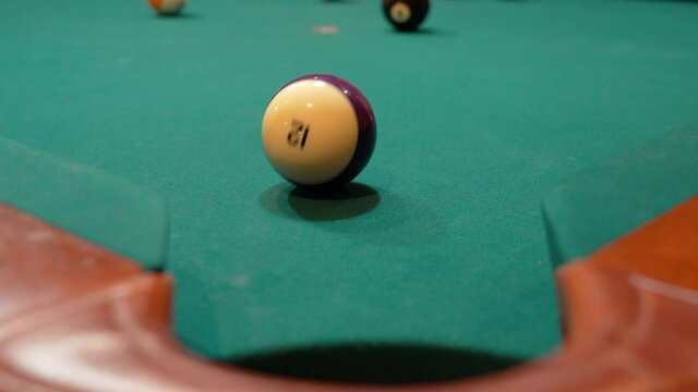 Pool Balls are Broken on an 8 Ball Triangle Rack and the Purple Stripe 12 Ball Slowly Rolls towards Edge of Corner Pocket, Closeup with Solids and Stripes Scattering Across the Table with Green Felt