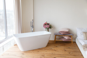Obraz na płótnie Canvas contemporary bathroom interior. Bathtub near a bed. Freshness and body care. Freestanding bathtub in the bedroom with wooden floor, console with cushions. Smart apartment