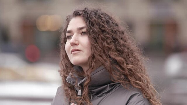 Portrait of a young woman with curly hair posing on a city street on a cold day.