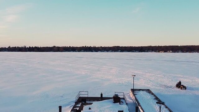 Fourwheeler ATV driving on frozen snow covered lake road during sunset; aerial