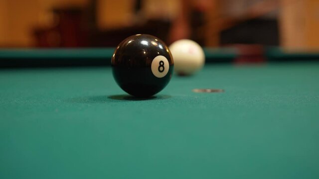 Man Playing 8 Ball Pool Gets Down and Shoots Solid Black Eight Ball into Pocket Past Camera using Draw or Backspin and Wooden Cue Stick on a Brunswick Table with Green Felt, Playing Billiard Bar Games