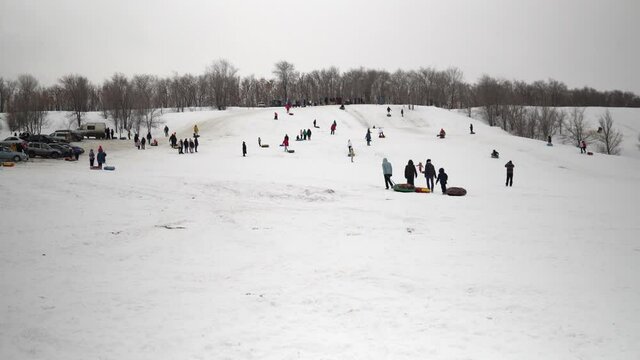 A crowd of people ride on snow slides. Children list themselves on the ice slide on inflatable rings. sledges, plastic skating rinks