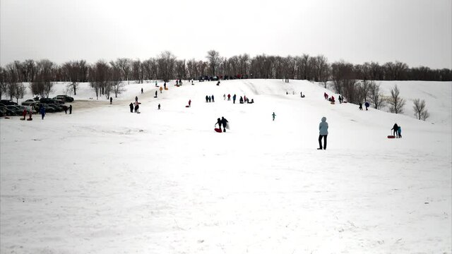 A crowd of people ride on snow slides. Children list themselves on the ice slide on inflatable rings. sledges, plastic skating rinks. Shooting time-lapse video