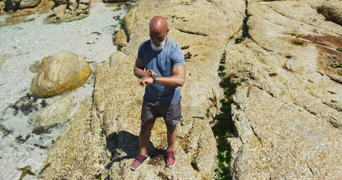 Senior african american man exercising using smartwatch on rocks by the sea