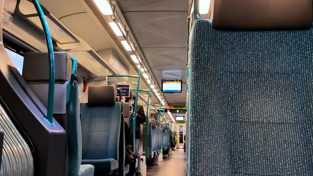 Slow pan right on railway train interior showing many empty seats and blurred people wearing masks on background