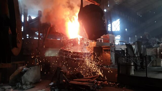 Hot liquid molten metal being poured from ladle into casting flask at steel fabrication industry. Slow motion.