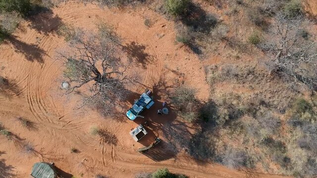Campsite in Kalahari red sand car under tree person sitting next to vehicle camera moving away to a high viewpoint