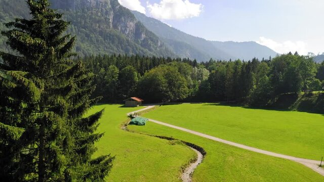 Gorgeous rising shot over a greenspace with a small river and path leading into the woods surrounding the mountains of the Bavarian Alps in Aschau im Chiemgau.