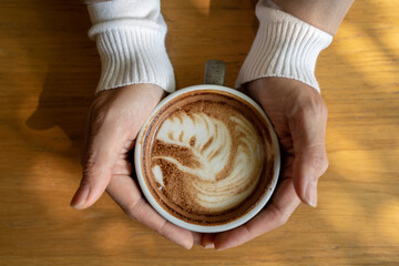 Female hands holding cup of coffee on wooden table top view. ,woman in white sweater holding a mug of coffee in the cold day