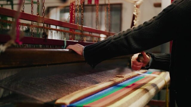 weaver weaving threads on traditional loom producing colorful textiles