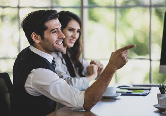 Portrait of a happy handsome young adult Caucasian businessman sitting in a multiethnics meeting at the conference room, pointing fingers with attractive smiling with a blurred businesswoman