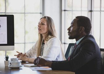 Professional middle-aged caucasian businesswoman sitting and concentrated listening to an idea in a multiracial business meeting. Selective focus at woman face with a blurred African businessman