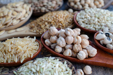 Closed up organic garbanzo bean in wooden spoon with blur soybean, lentil, pearl barley, flax seeds, rice, barley, mung, and sesame on grunge wooden background in soft brown tone