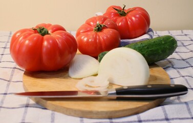 Red large tomatoes, onion white and knife for cutting on wooden board