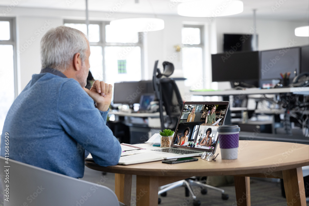 Wall mural Caucasian man in office having video call with colleagues displayed on laptop screen