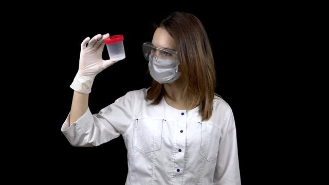 Young woman doctor checks sperm tests. The woman examines the test jar, then shows a thumb down. Negative sperm analysis. On a black background.
