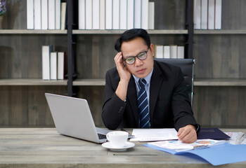 Fototapeta premium Sad Asian businessman touch his temple with one hand, sitting in the office. The concept of unemployed, sadness, depressed and human problems.