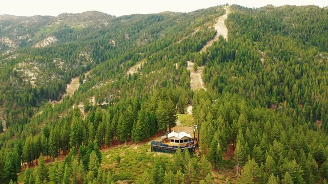 A circling panoramic view of a lodge at the top of ski slope during the summer months at Lake Tahoe in California. The drone circles capturing 4k video with the forest conquering the picture.