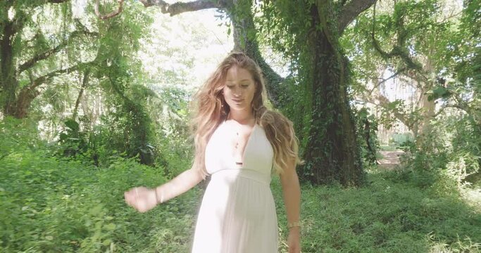 Forest fairy, smiling blonde girl in white dress walks in lush jungle