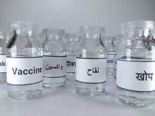 Closeup shot of vaccine bottles and the word vaccine written on them in Nepali, Arabic, Bangali, Pashto, English 