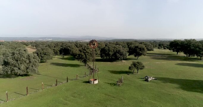 Aerial video Old wind power pump in Spanish farm surrounded by holm oaks