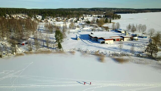 Two people skiing on a frozen lake on a cold sunny day. Forward dolly aerial footage.