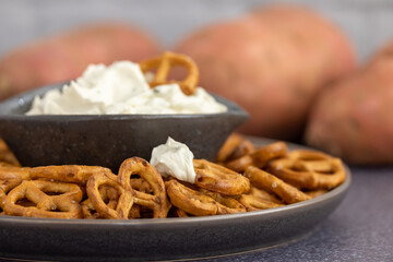 Close up of healthy sweet potato pretzels in a tray with chive and onion cream cheese dip on a dark table and a white background.

