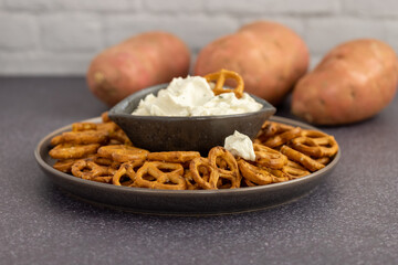 Healthy sweet potato pretzels in a tray with chive and onion cream cheese dip on a dark table and a white background.
