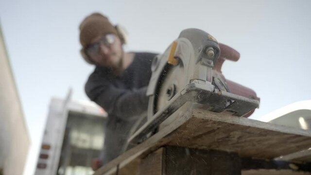 Carpenter cutting wood with circular saw, close up low angle, focus on saw