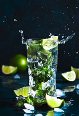 Mojito with splash and drops. Cocktail or mocktail with lime, mint, and ice in glass on blue background. Summer cold alcoholic non-alcoholic drink,  beverage and cocktail. Copy space