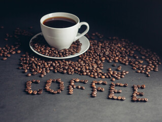 cup with a fragrant drink on a dark background heart of coffee beans white saucer