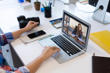 Caucasian woman in office having video call with diverse colleagues displayed on laptop screen