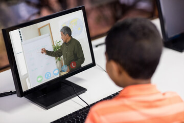 Fototapeta na wymiar Mixed race schoolboy using computer on video call with male teacher