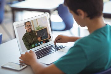 Caucasian schoolboy using laptop on video call with male teacher