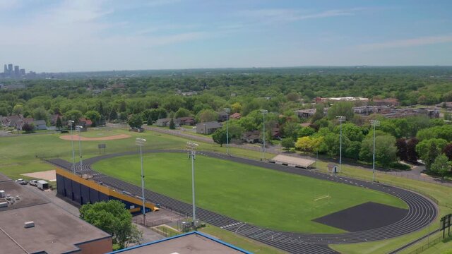 High school bleachers and track in residential neighborhood with city skyline on the horizon- aerial drone flyover shot