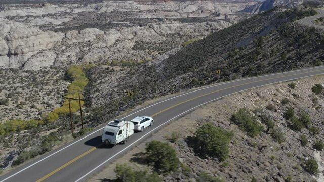 Domestic Tourists in Crossover SUV Tows Camper Trailer Along Winding Scenic Byway Following Exposed Mountain Ridge in Escalante Utah