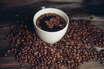 coffee beans scattered on a wooden table and a cup with a hot drink aroma
